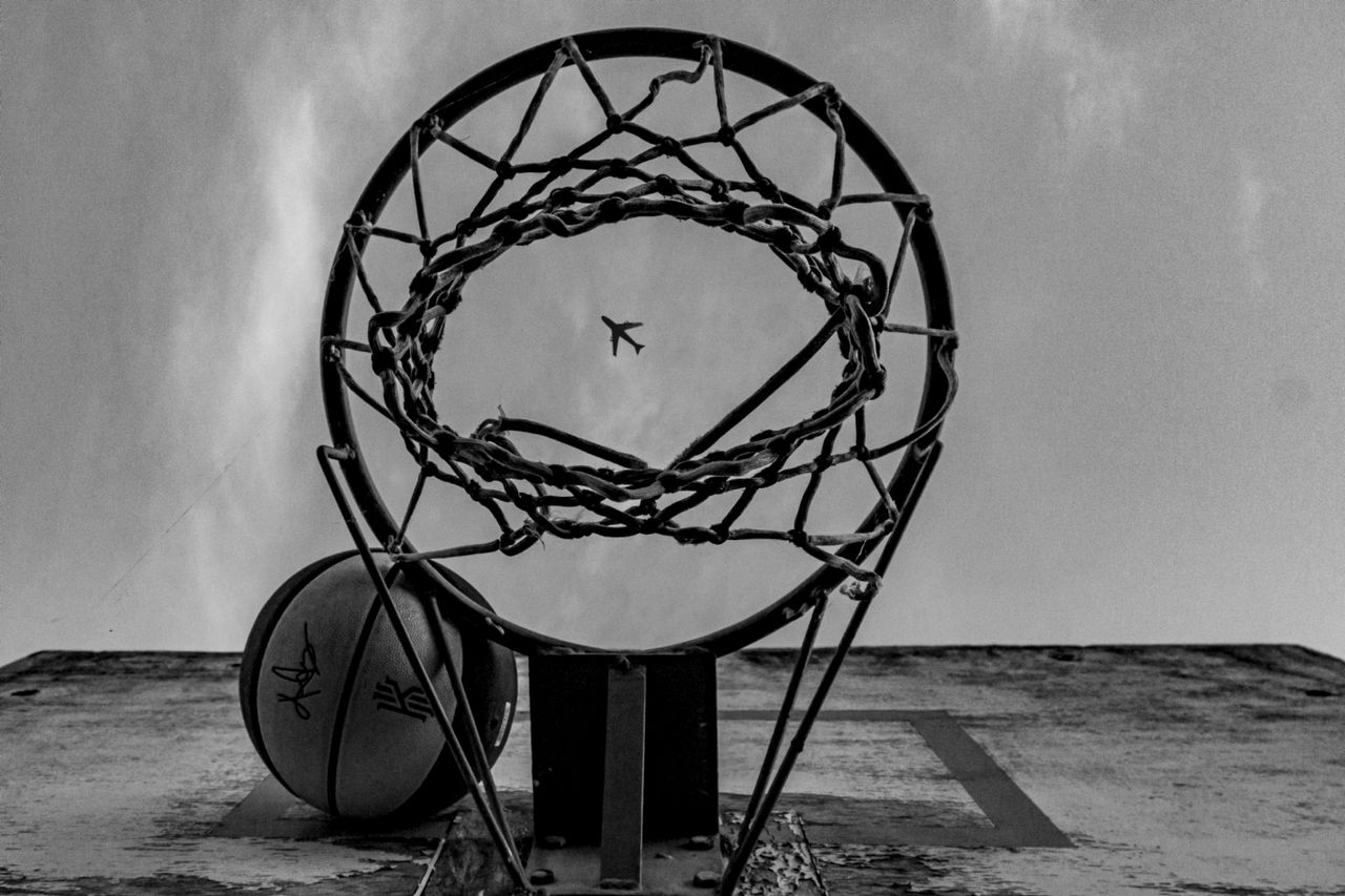 bedroom-bliss Black and white image capturing a unique view of a basketball hoop with an airplane in the sky.